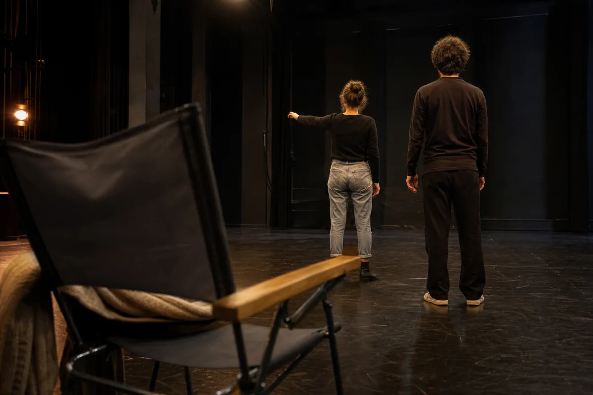 Répétition sur un plateau nu, deux comédiens de dos travaillant une scène près d&rsquo;une chaise de metteur en scène